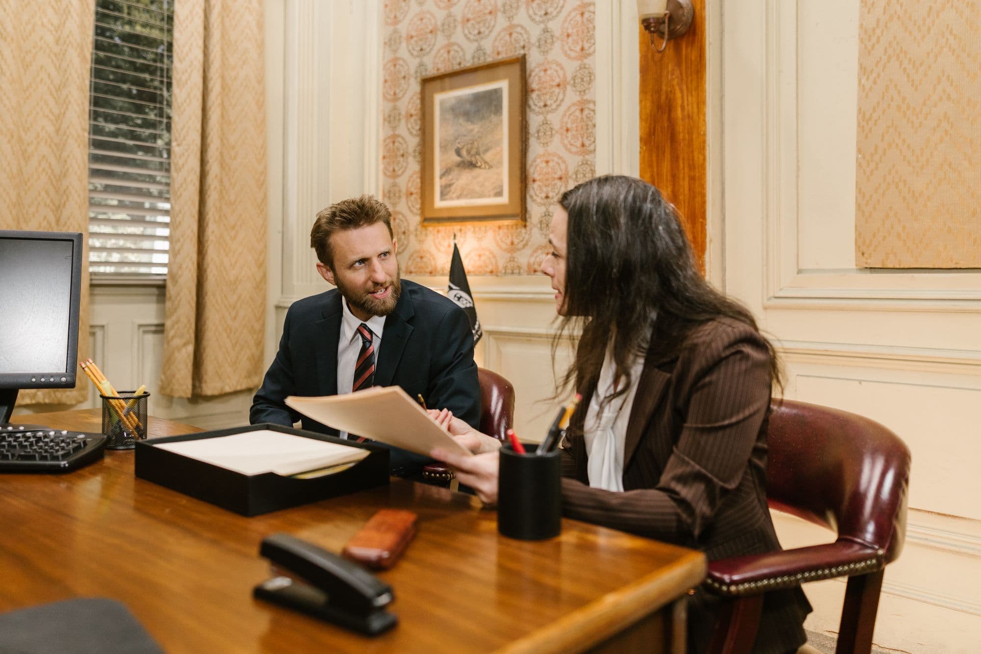Two people talking across a wooden desk in a wood-panelled office