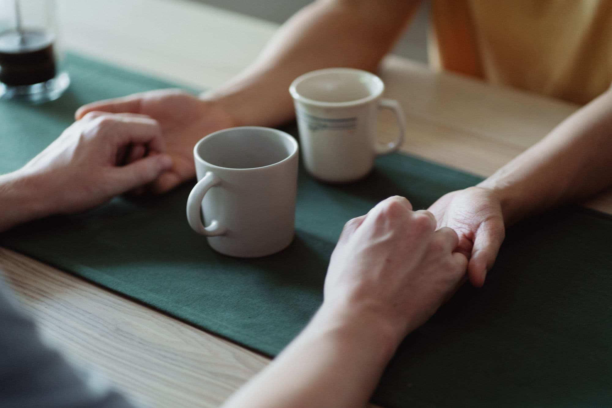 Two people holding hands across a table, beside two mugs