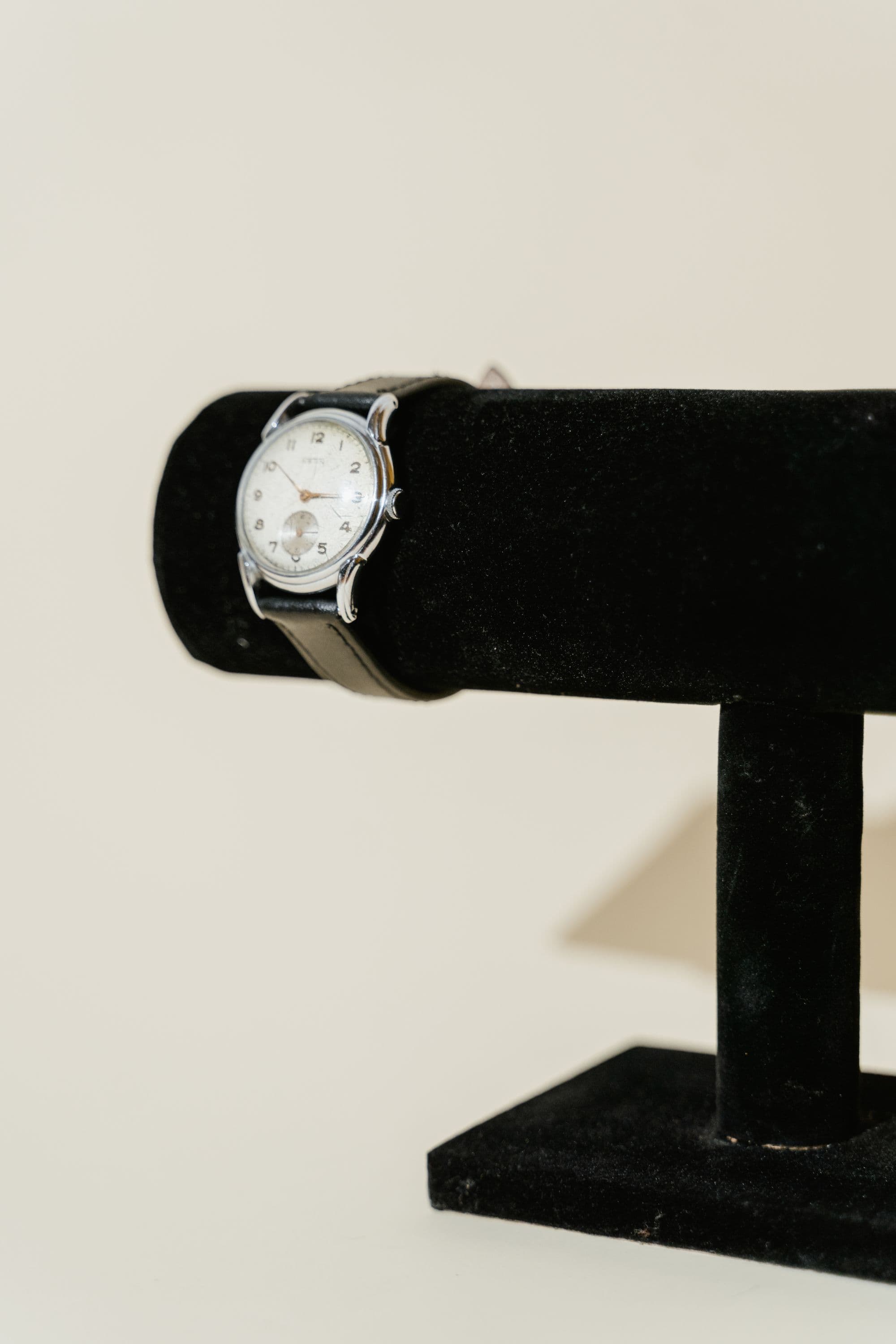 A wristwatch with a white dial on a black velvet stand